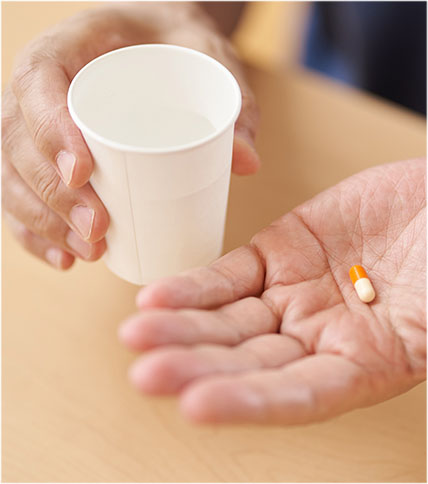 Hand holding a cup and the other hand holding a pill.