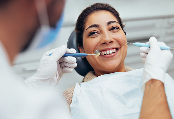 Woman in operatory chair smiling with dentist holding dental tools near mouth.